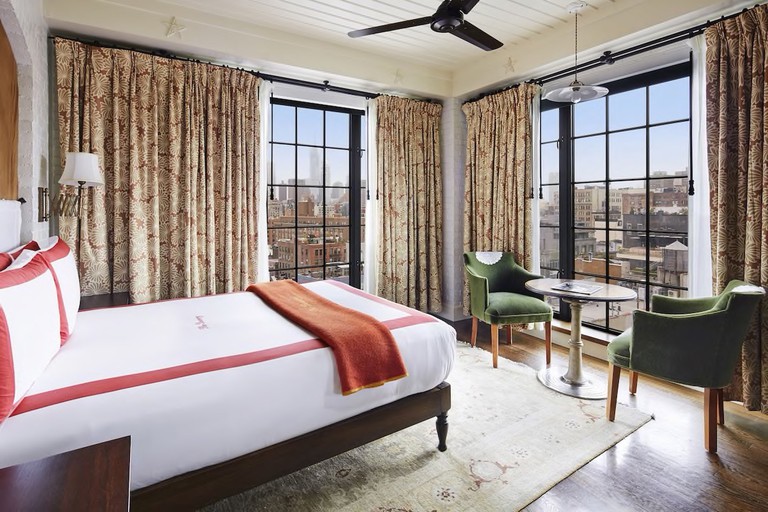 A bedroom at The Bowery Hotel has floor-to-ceiling windows on two sides offering panoramic views over lower Manhattan.