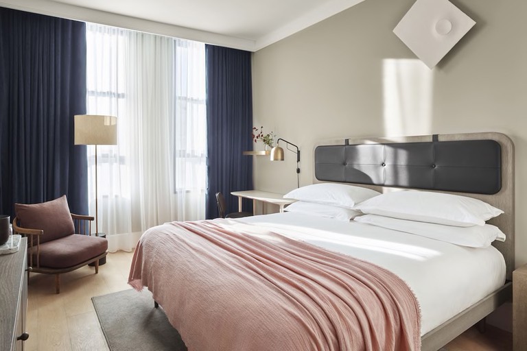 A large contemporary hotel room with chic soft furnishings in blush tones and crisp white bed linen at 11 Howard.